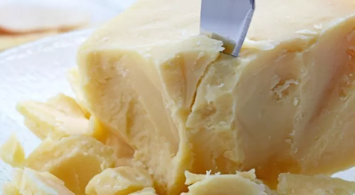 Нож разрезает рассыпчатый кусок пармезана.