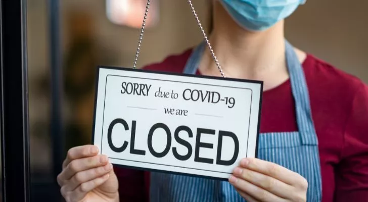 Женщина в маске надевает "закрыто из-за COVID-19" подпишись в окне